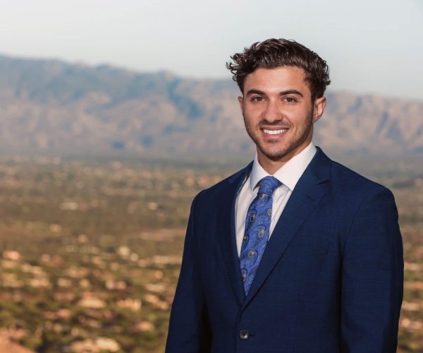 A Man Wearing A Suit And Tie Standing In Front Of A Mountain