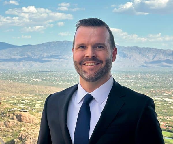 A Man Wearing A Suit And Tie Standing In Front Of A Mountain